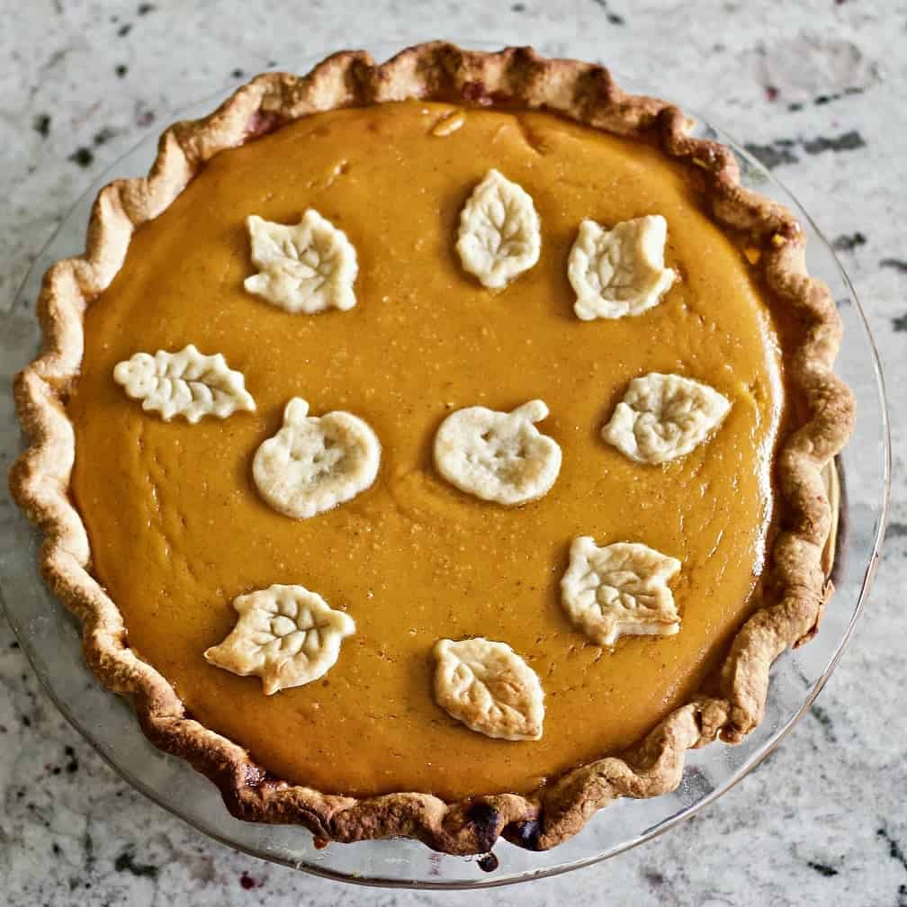 Pumpkin pie with dough cut outs on top two pumpkins and fall leaves bake in to celebrate the season