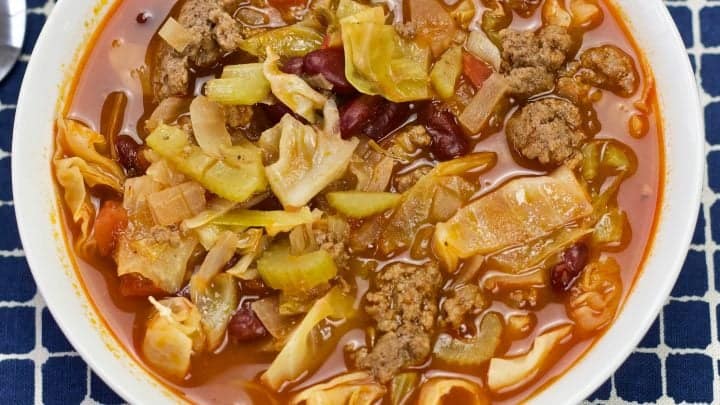 Cabbage soup in a white bowl on a blue plaid cloth