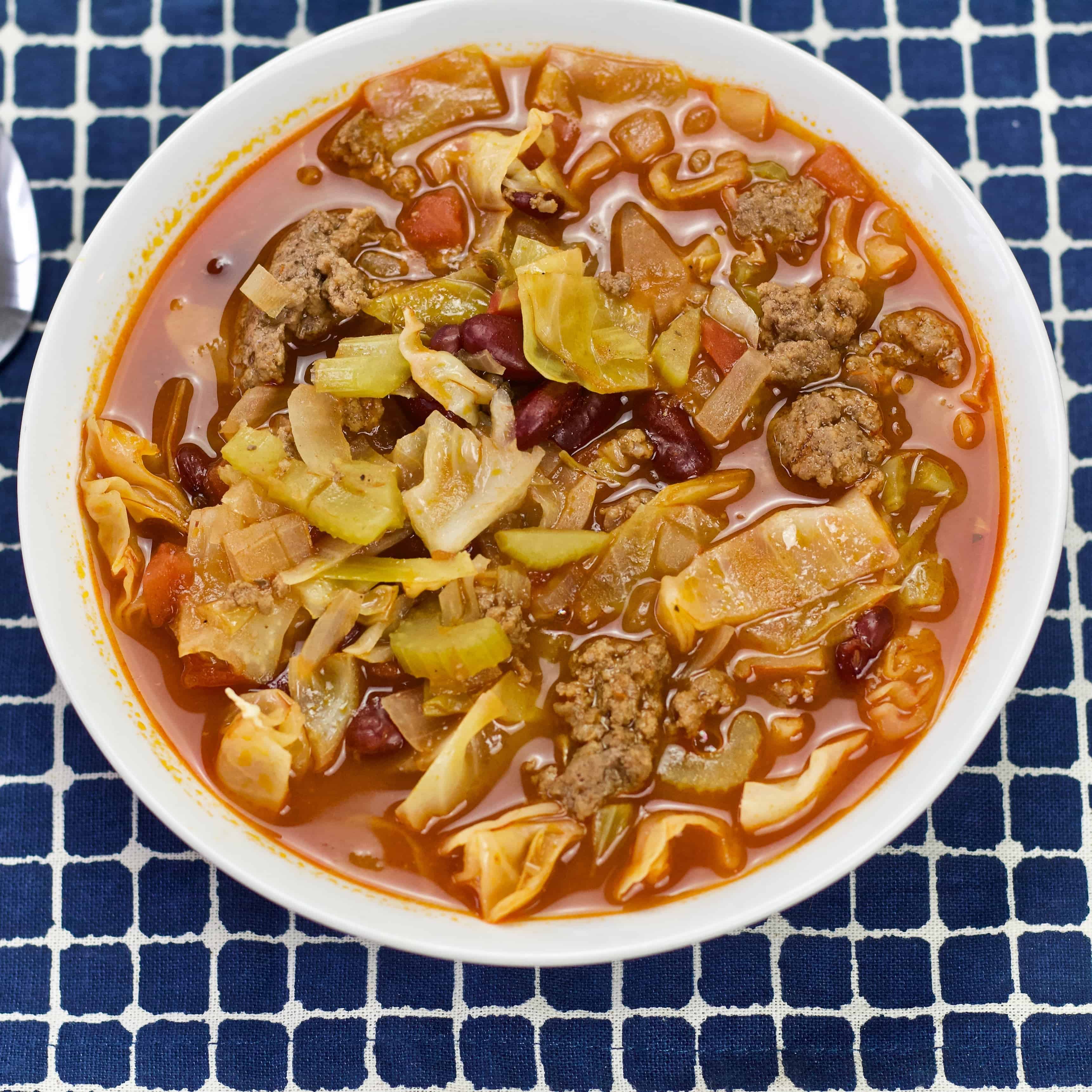 Cabbage soup in a white bowl on a blue plaid cloth