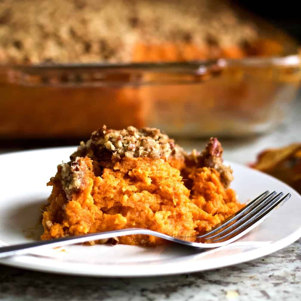 Sweet Potato Casserole with a Pecan Topping 2 Sweet Potato Casserole serving on a white plate with the casserole dish in the background.