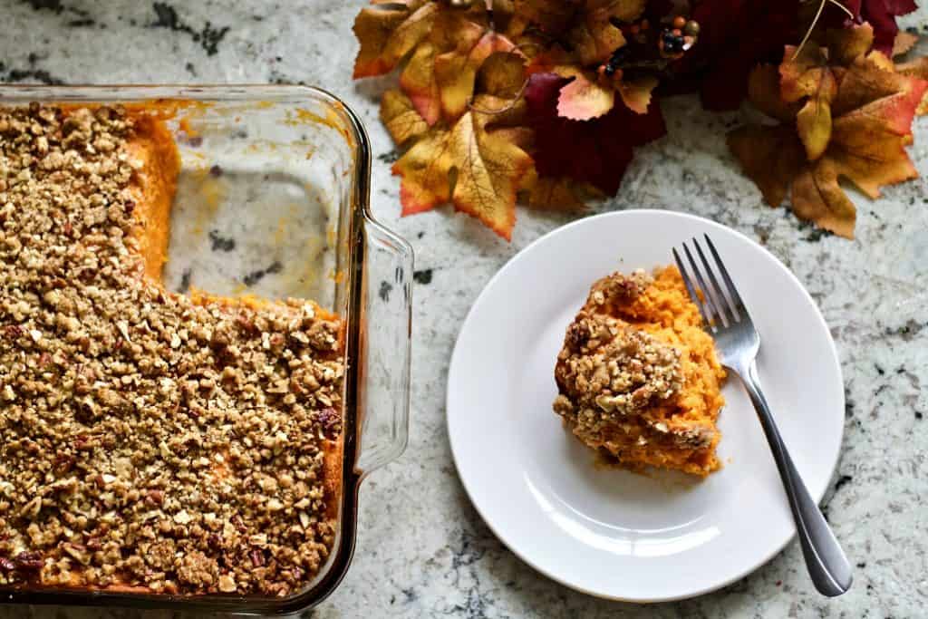 Sweet Potato Casserole with a Pecan Topping 4 Sweet Potato Casserole top down look of the casserole with one serving removed and set on a plate at the side.