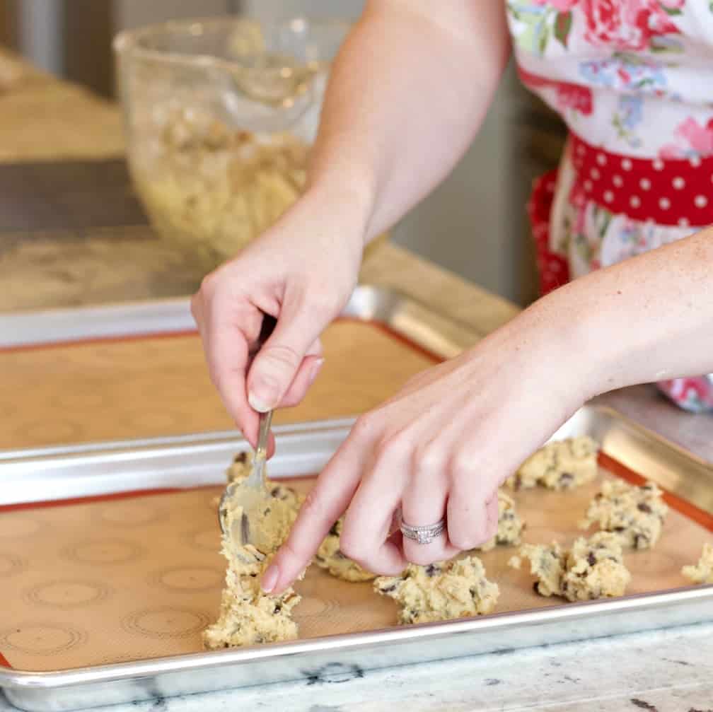Creamy Chocolate cookie dough being dropped by teaspoonfuls onto the cookie sheet covered in a silicone mat.