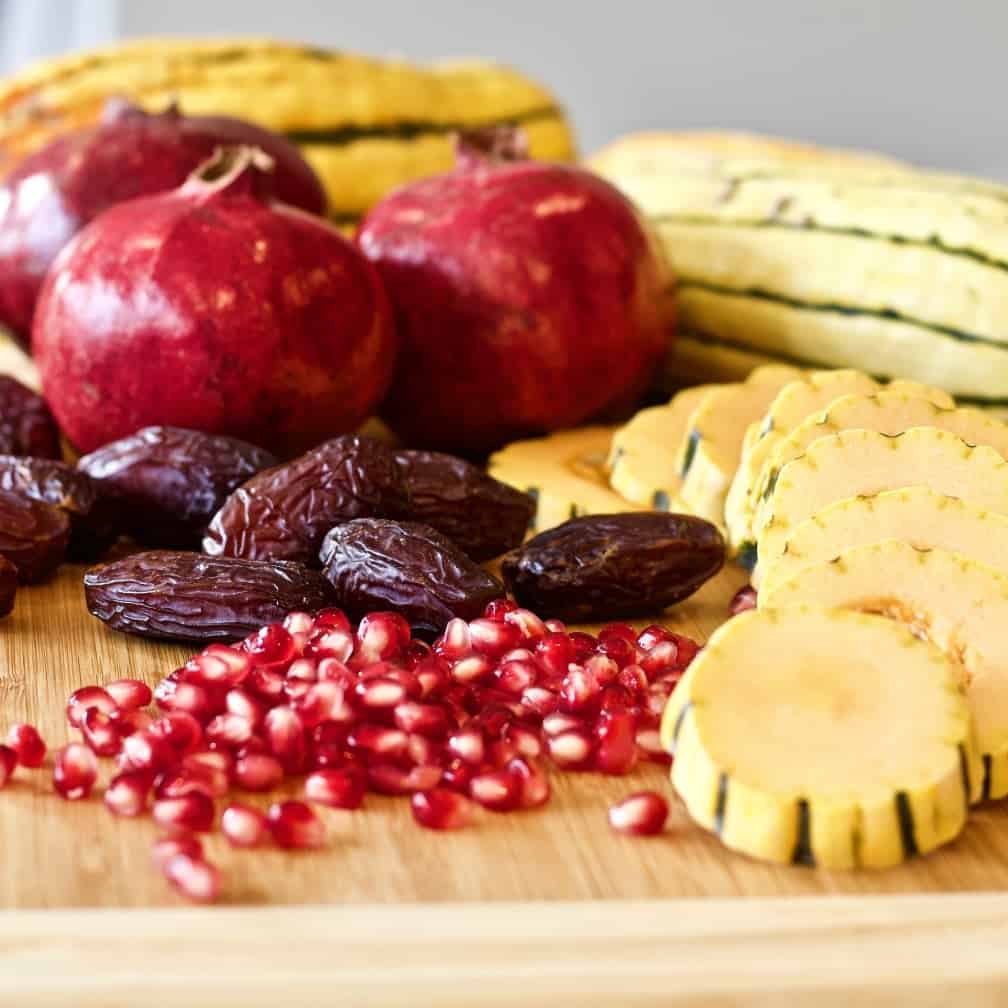 Delicata squash, pomegranate, and medjool dates on a cutting board.