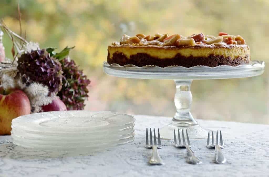 Apple Cheesecake on cake stand resting on a dessert table with fall decorations.
