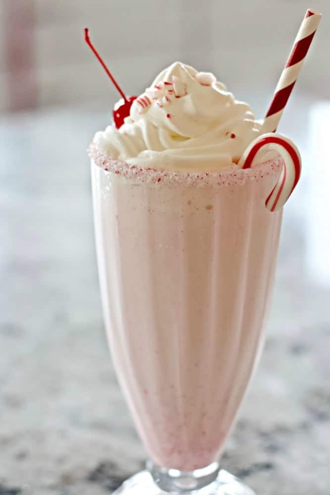 Peppermint Schnapps Milkshake in a soda glass garnished with whipped cream, a candied cherry, crushed peppermint candy, a mini candy cane and straw.