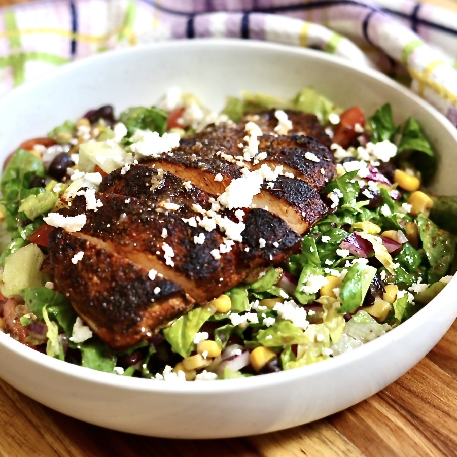 blackened chicken salad with corns and beans in a white serving size bowl chicken arranged on top