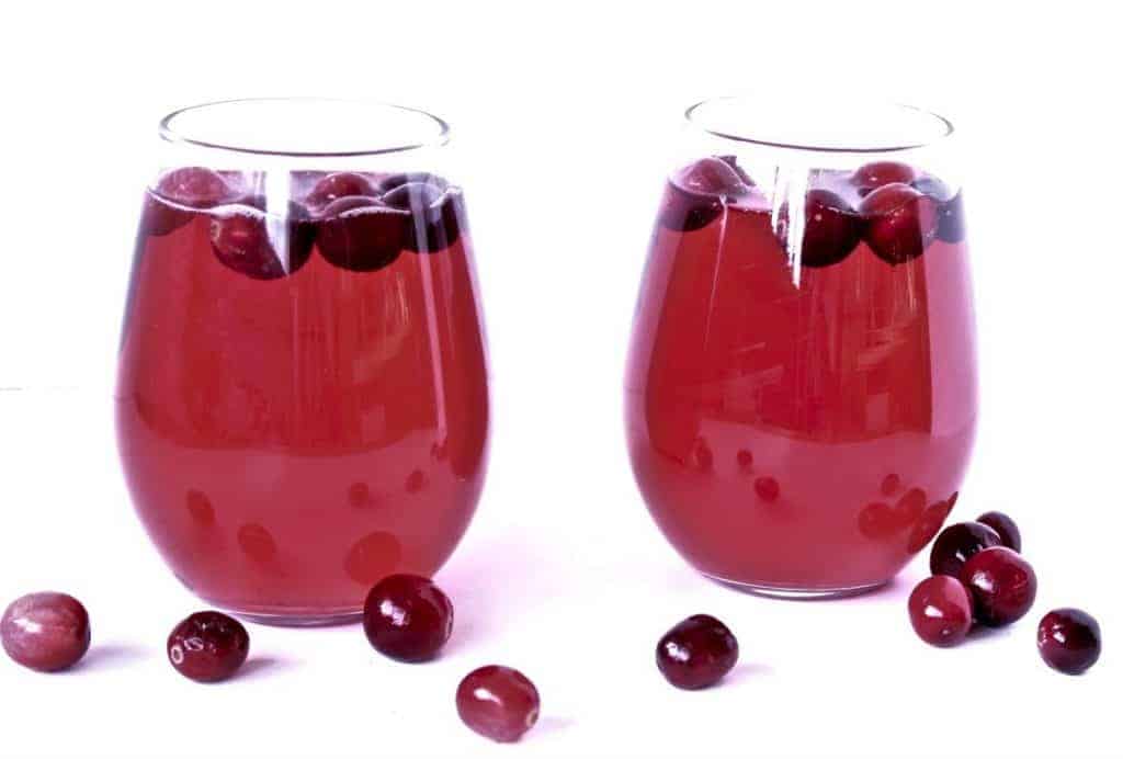 Cranberry Mimosas with fresh cranberries in two stemless glasses.