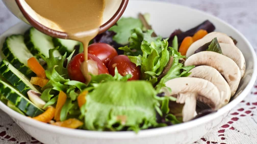 pouring creamy balsamic dressing onto a salad.