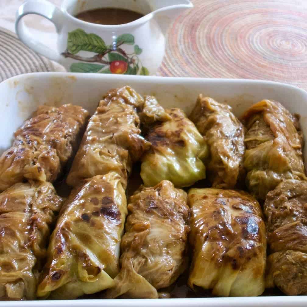 Cabbage rolls in a serving dish with gravy in a gravy server