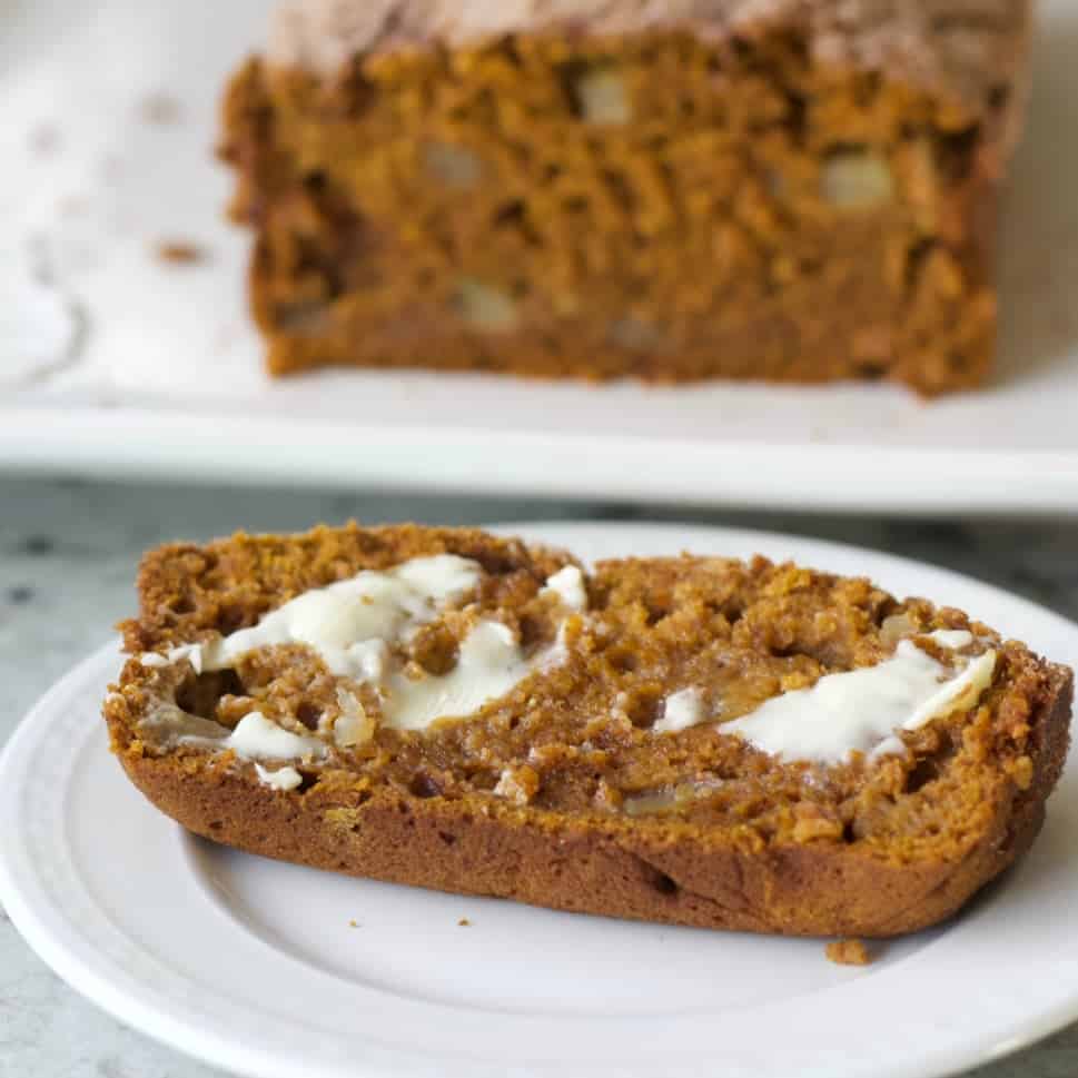 Pumpkin Apple Spice Bread warm single slice on a white plate with melting butter.