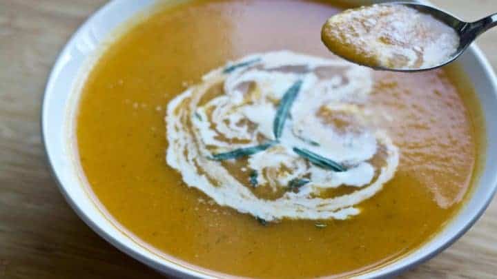 Carrot Tarragon Soup garnished with fresh tarragon and cream in a white bowl