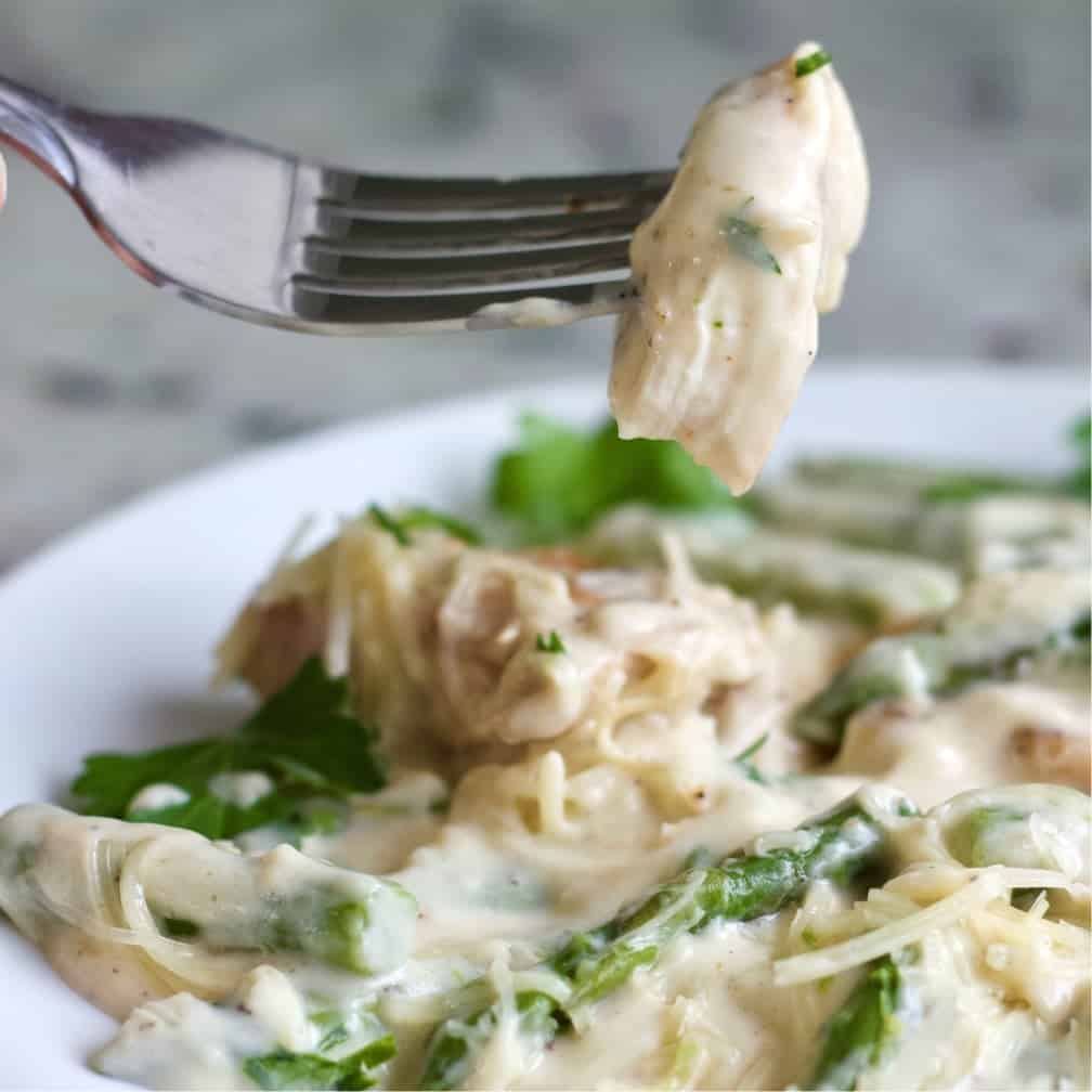 chicken alfredo asparagus dinner serving with a forkful of creamy coated chicken.