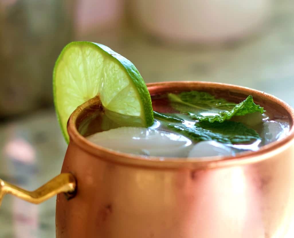 Moscow mule vodka drink in a copper mug with lime and mint leaves.