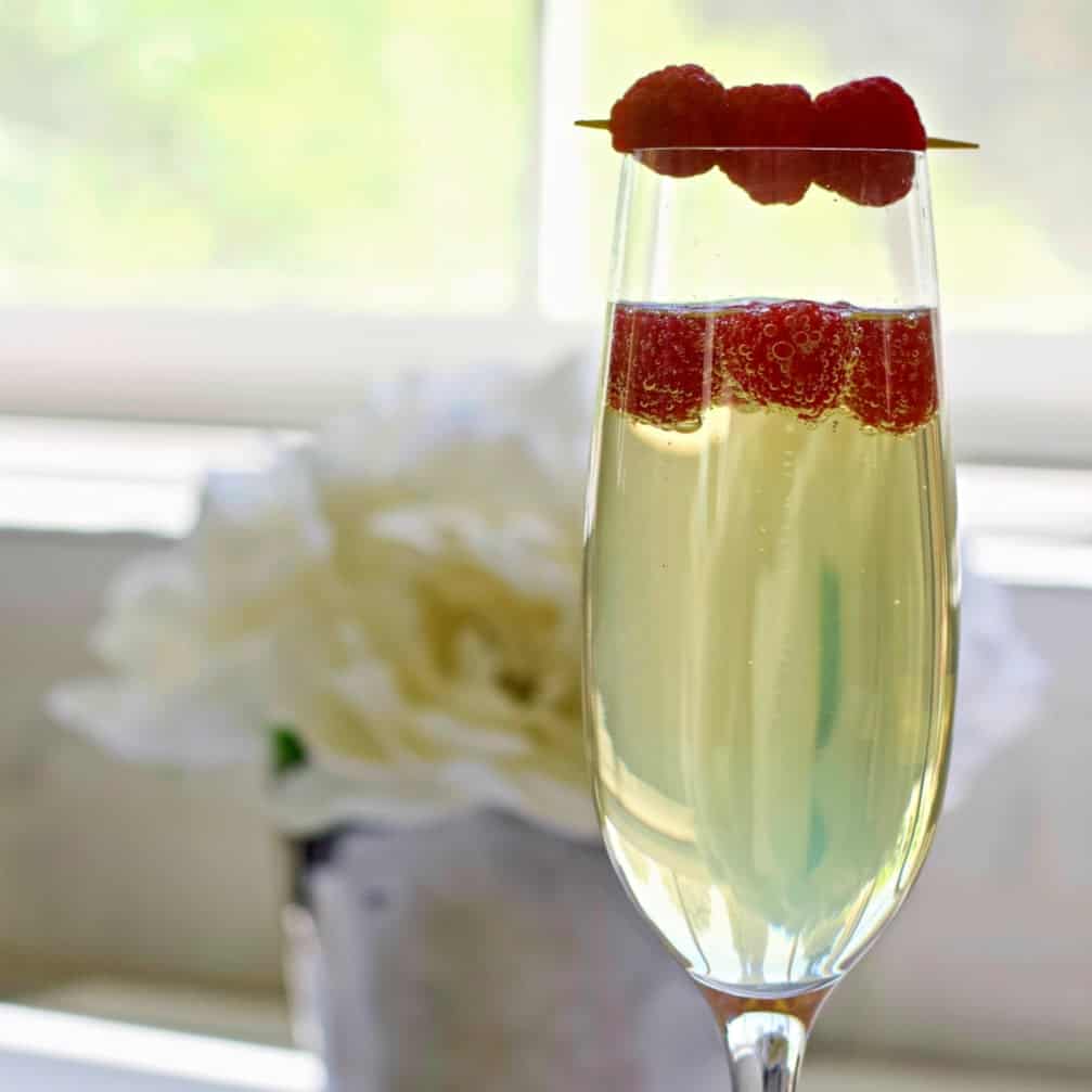Easy and Delicious Rosé Sangria Recipe 8 Limoncello prosecco garnished next to a white flower in front of a window.