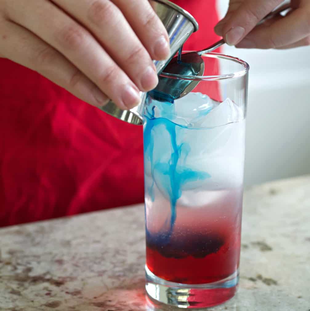 adding the cura&ccedil;ao layer by pouring it over the back of a spoon into the glass.