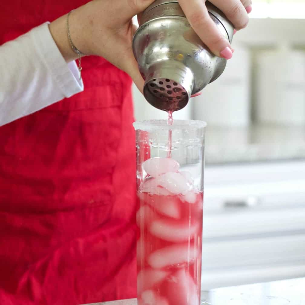 Pouring the shaker ingredients into a Collins glass