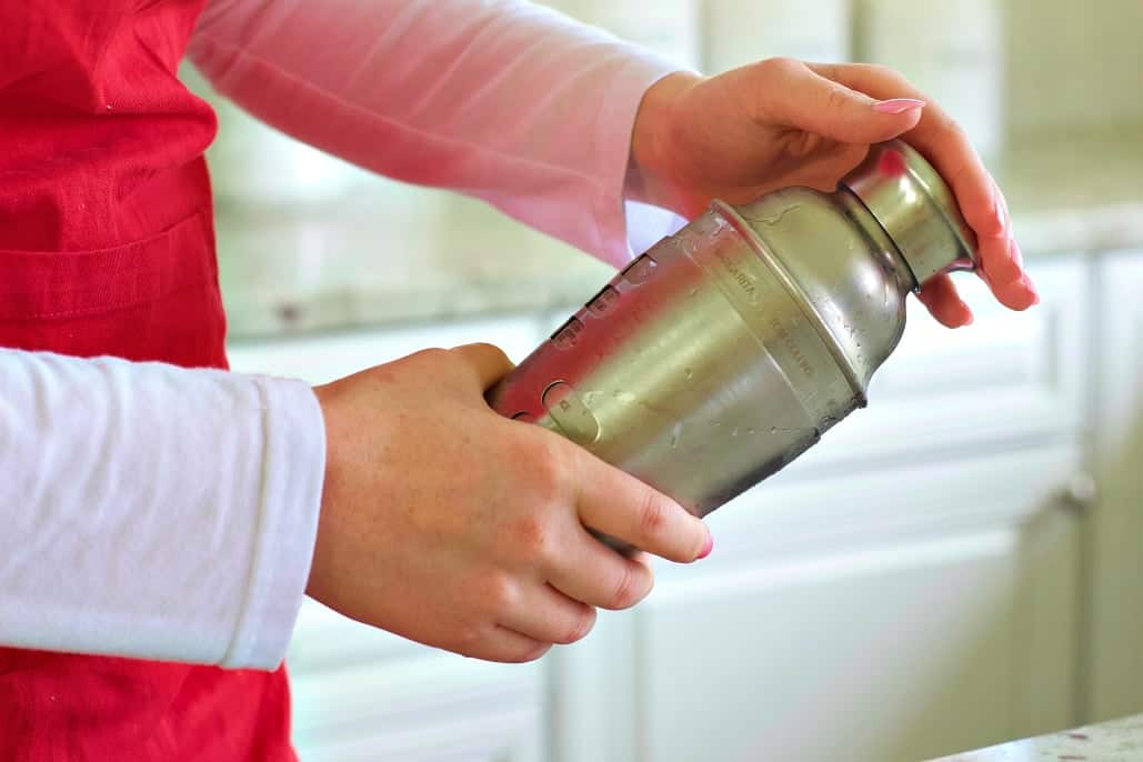 shaking a cocktail shaker with ingredients for the Pink Lemonade.