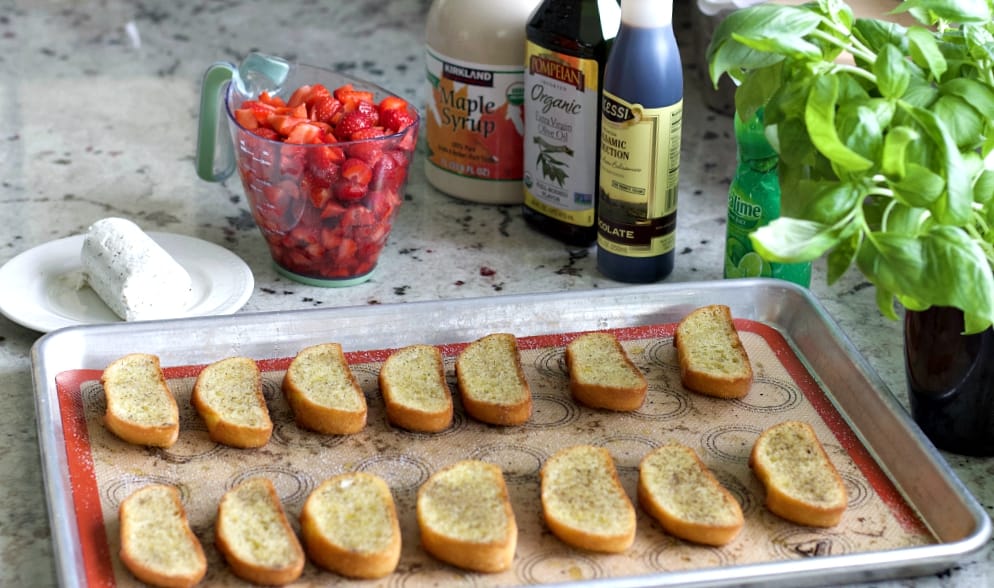 bruschetta bread slices on a baking sheet surround by the ingredients for this recipe.