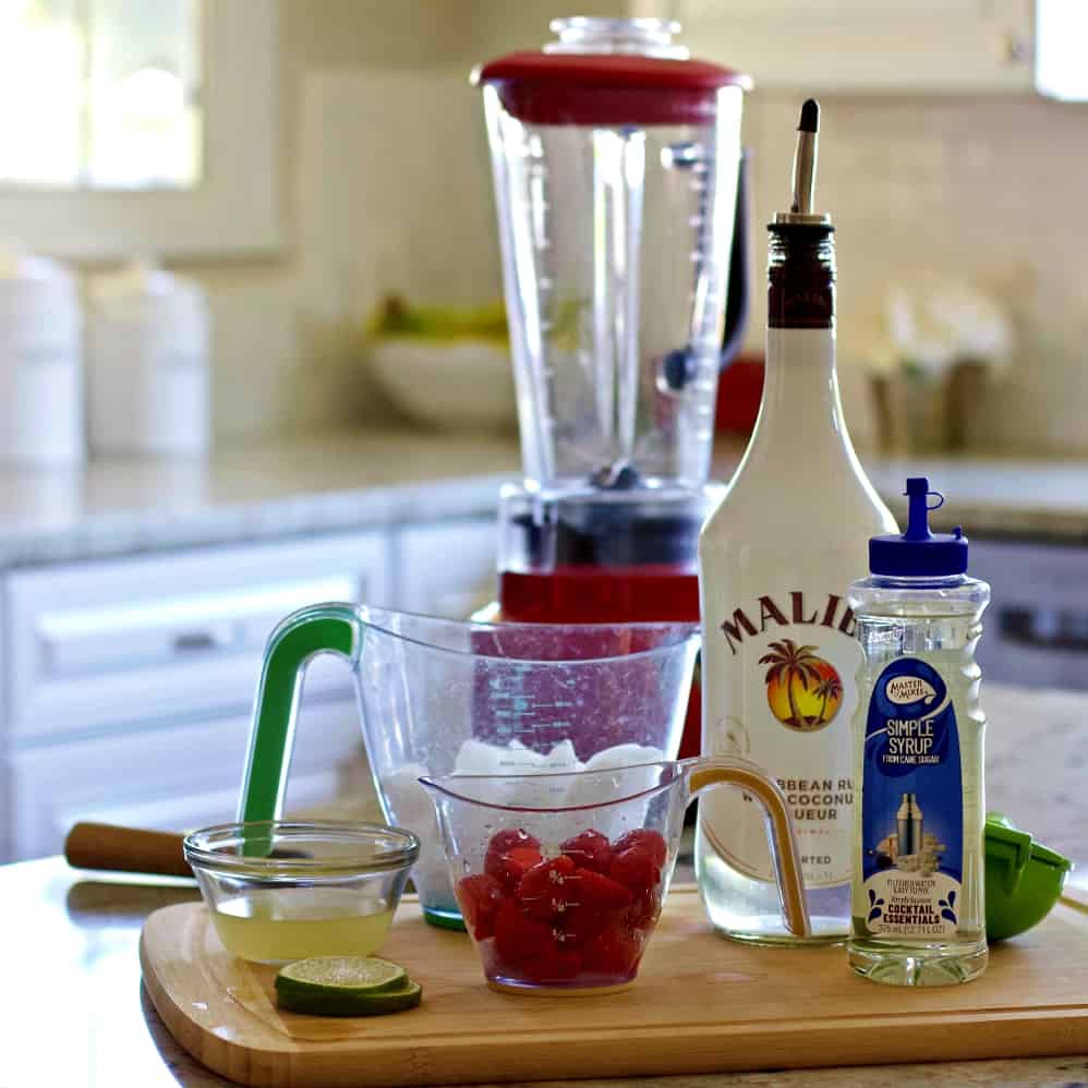 Strawberry Daiquiri Recipe with Malibu Coconut Rum 4 The ingredients for this drink sitting on a wooden board with a blender.