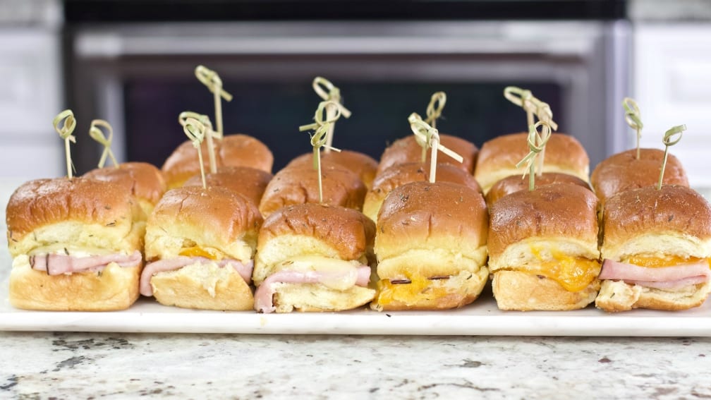 side shot of ham and cheese sliders with bamboo picks and on a party tray.