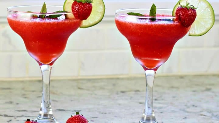 two strawberry daiquiris garnished with lime wheels and whole strawberries