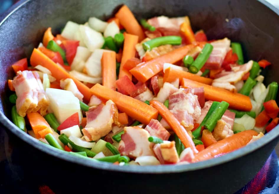 vegetables and bacon cooking in a skillet