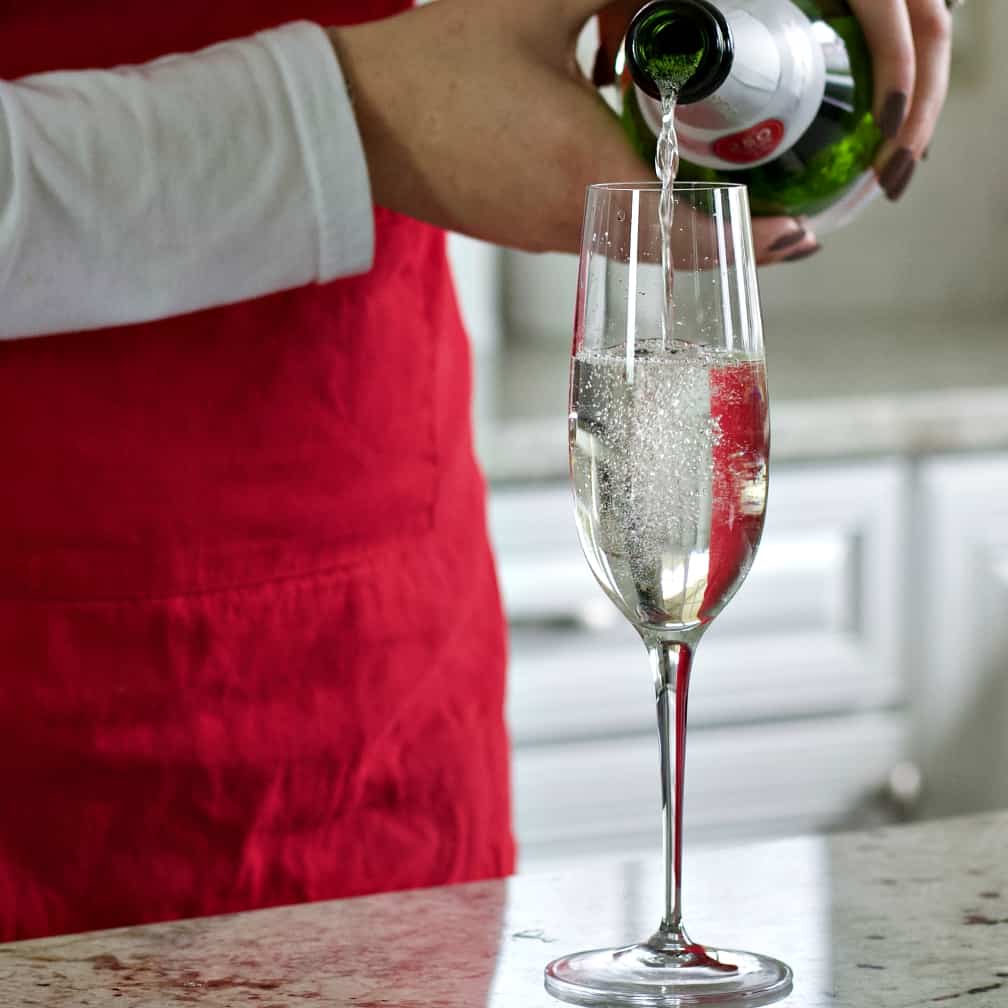 White Cranberry Mimosa Recipe with Rosemary 10 pouring Sparkling wine into a champagne flute