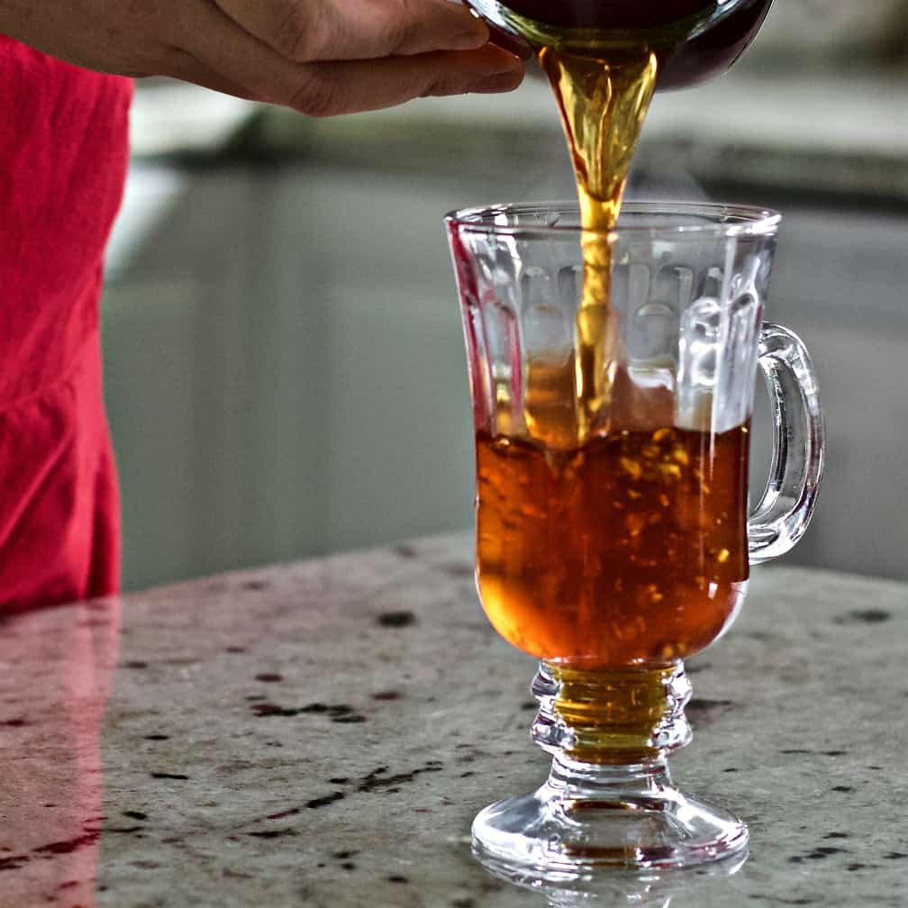 Pouring hot coffee into a clear mug.