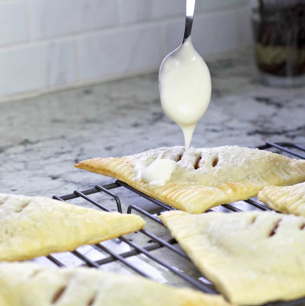 Homemade Apple Turnover Recipe with Puff Pastry 23 drizzling glaze on apple turnover.