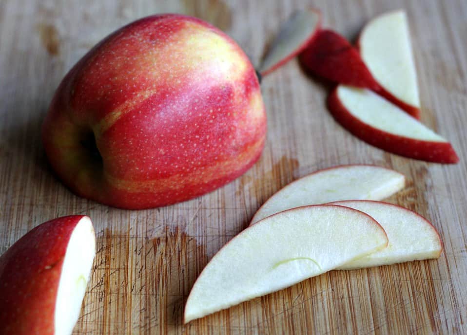 Cut apple slices with half a red apple on wooden cutting board.
