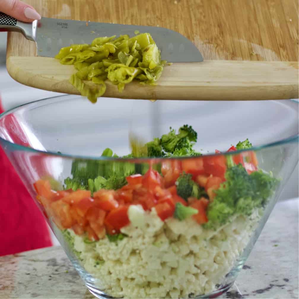 sliding chopped pepperoncini into salad bowl-cauliflower salad