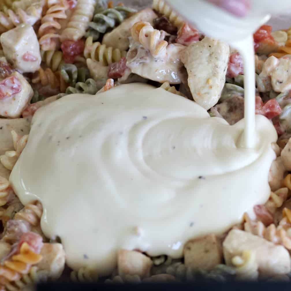Chicken Bacon Ranch Casserole Recipe 7 pouring alfredo sauce over pasta and chicken