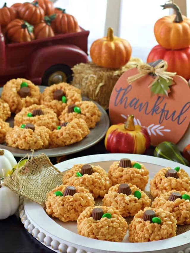 pumpkin rice krispie treats on white and metal trays on themed table