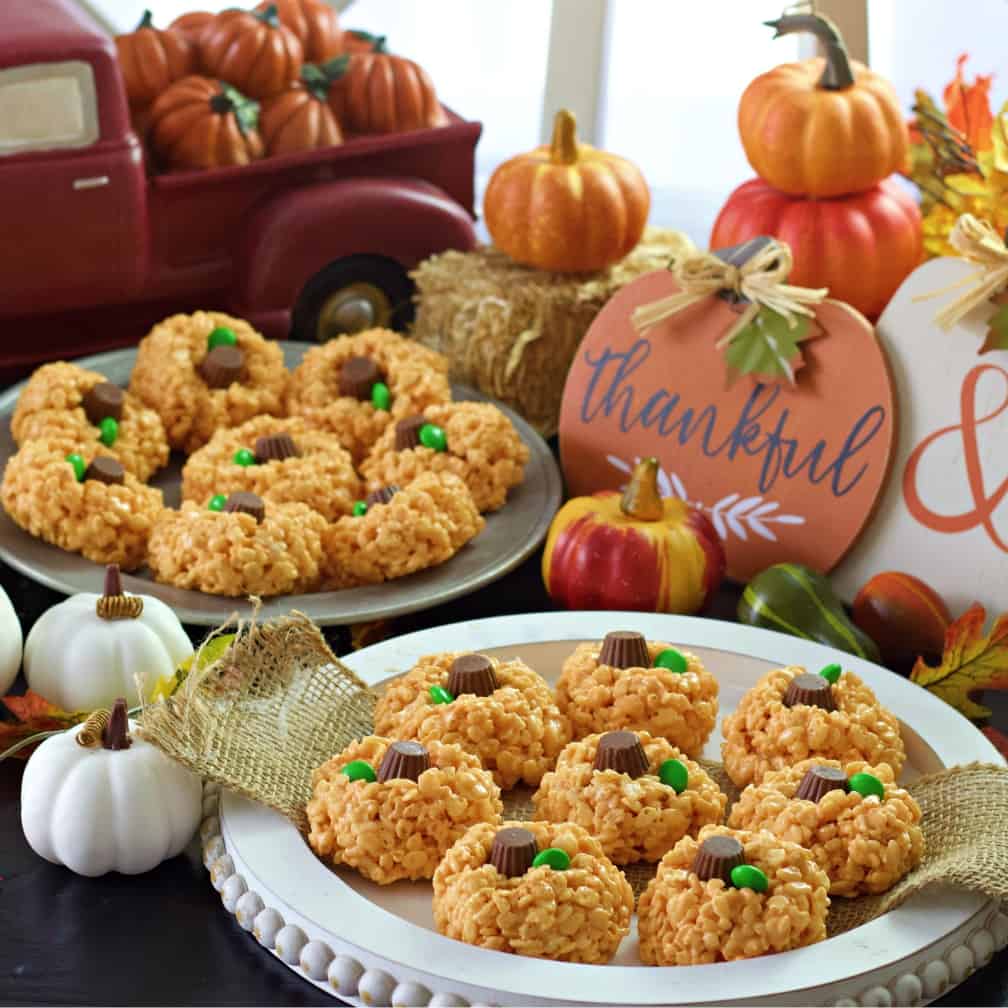 pumpkin rice krispie treats on white and metal trays on themed table