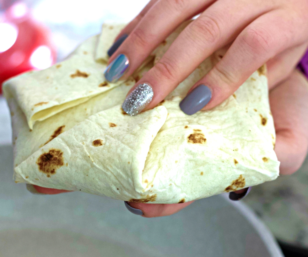 holding a folded raw crunchwrap supreme