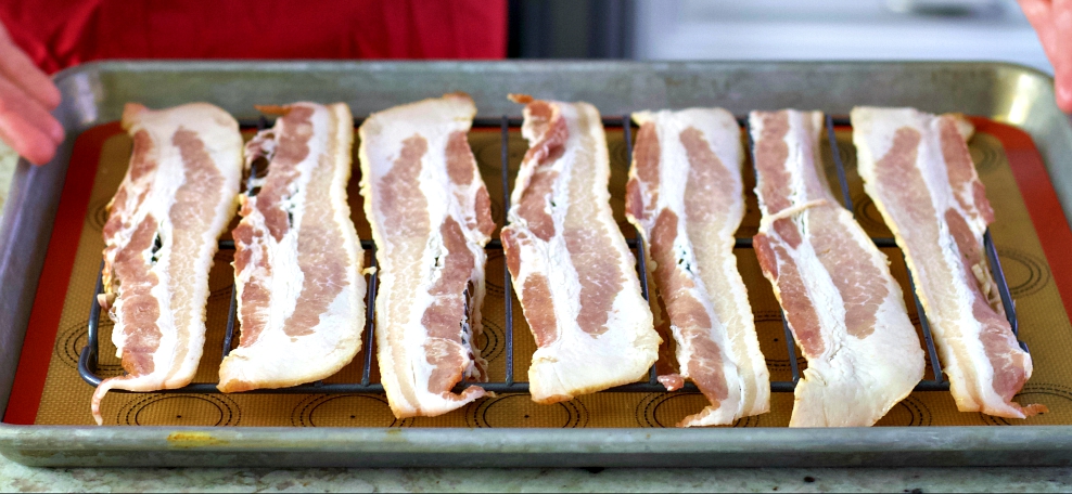 raw bacon strips on a baking tray