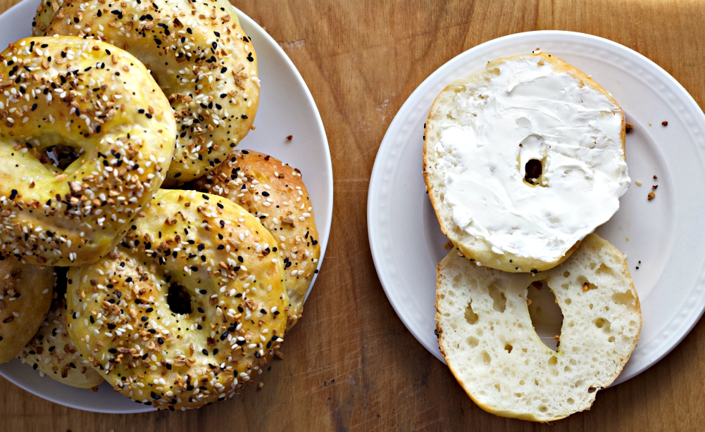 cream cheese on cut bagel half with stack of bagels
