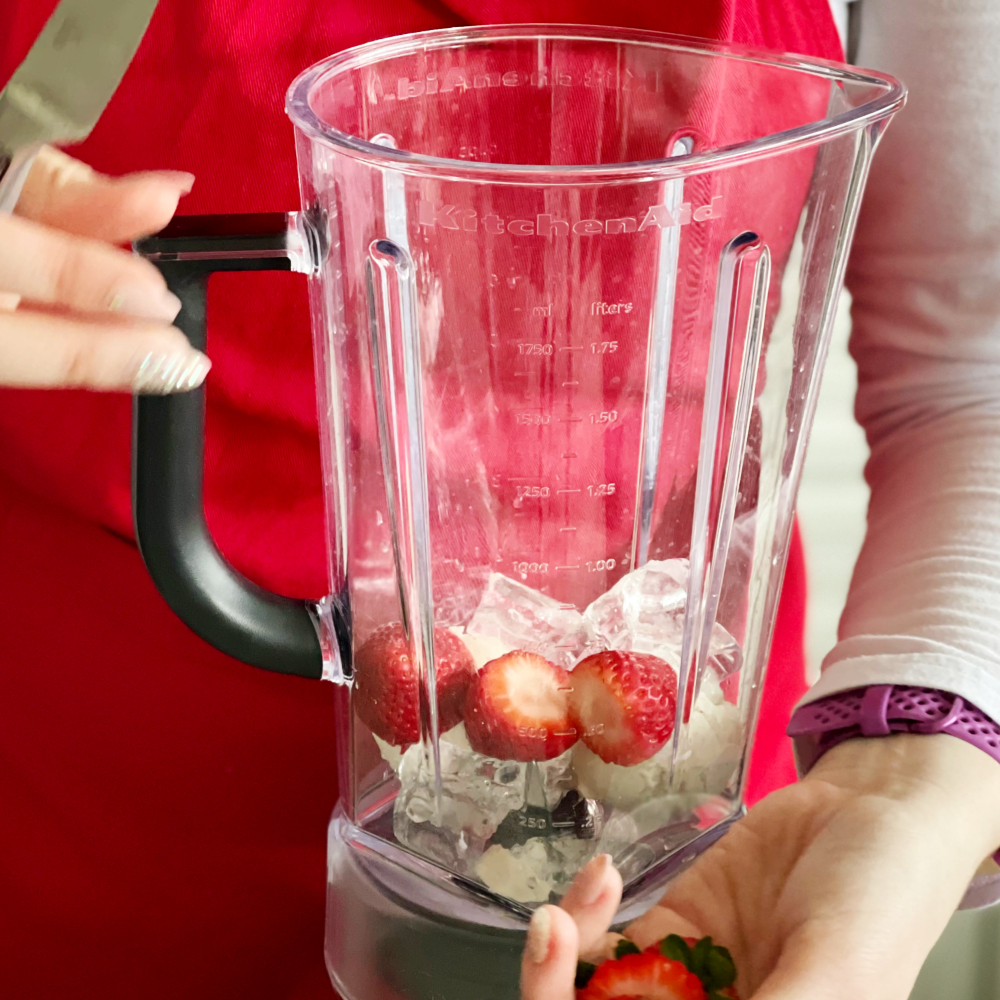 adding cut strawberries into blender