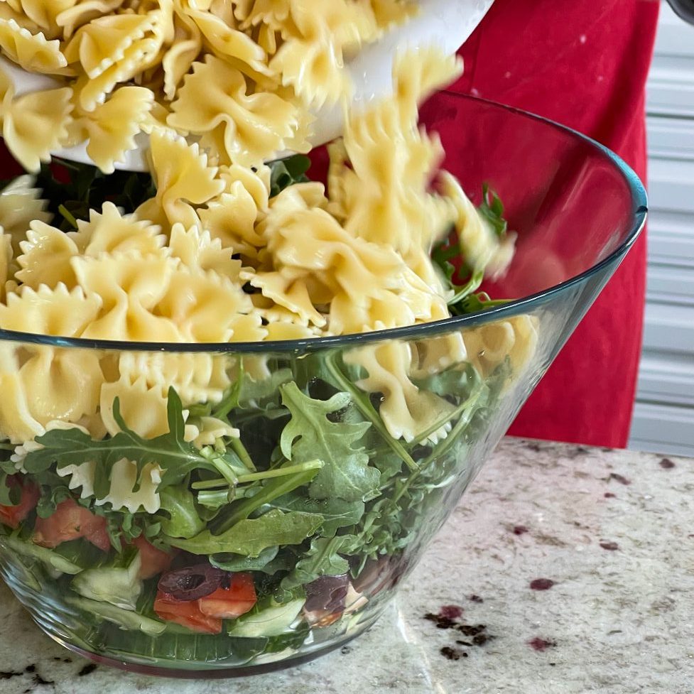 adding pasta to Mediterranean salad