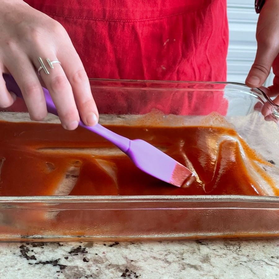 spreading enchilada sauce on bottom of casserole dish