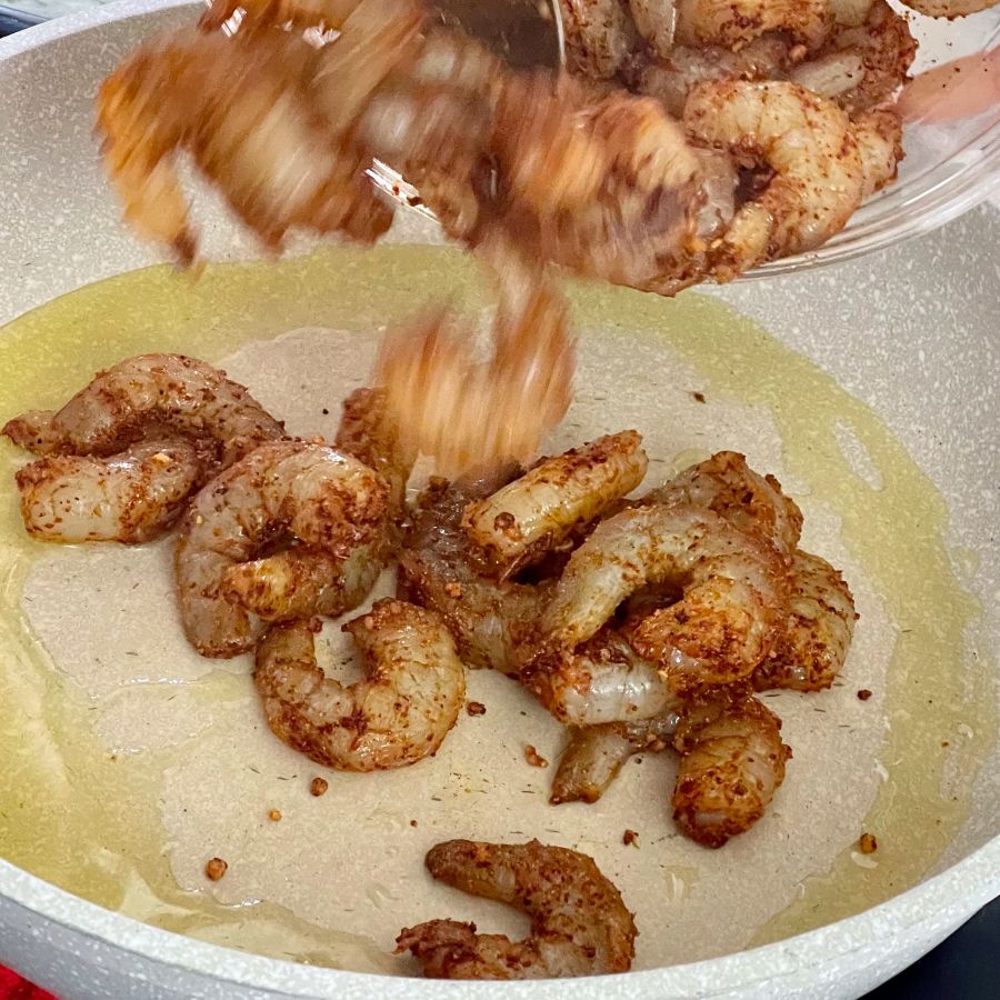 pouring seasoned shrimp into hot fry pan.