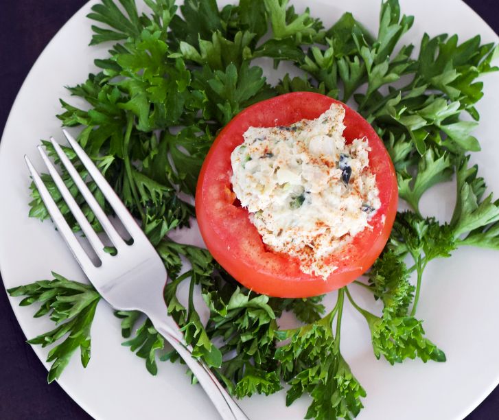 stuffed tomato on a white plate with curly parsley
