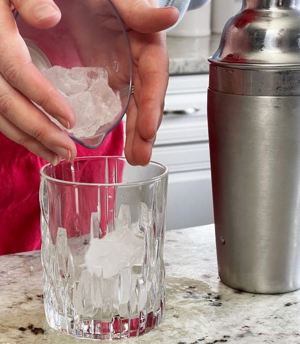 pouring ice into whiskey glass-crown royal maple cocktail