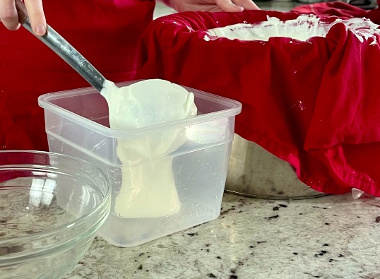 scooping sieved Greek Yogurt into container
