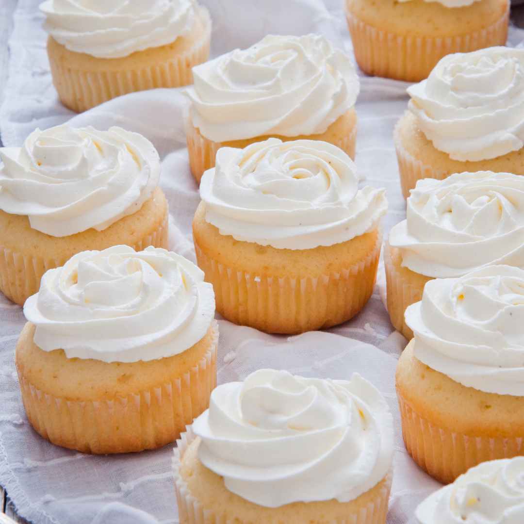 a group of vanilla cupcakes on parchment with white buttercream frosting