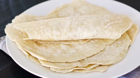 sourdough tortillas stacked on a plate with top one rolled