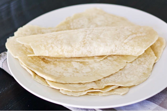 sourdough tortillas stacked on a plate with top one rolled