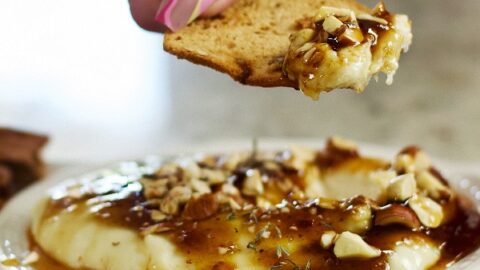 dipping a cracker into whipped brie on a plate
