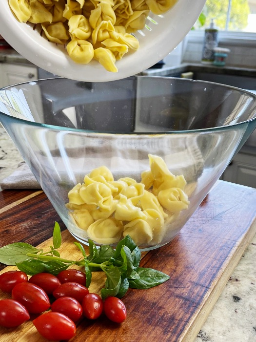 pouring cooked tortellini into salad bowl