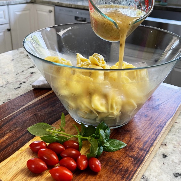 pouring dressing onto tortellini in salad bowl